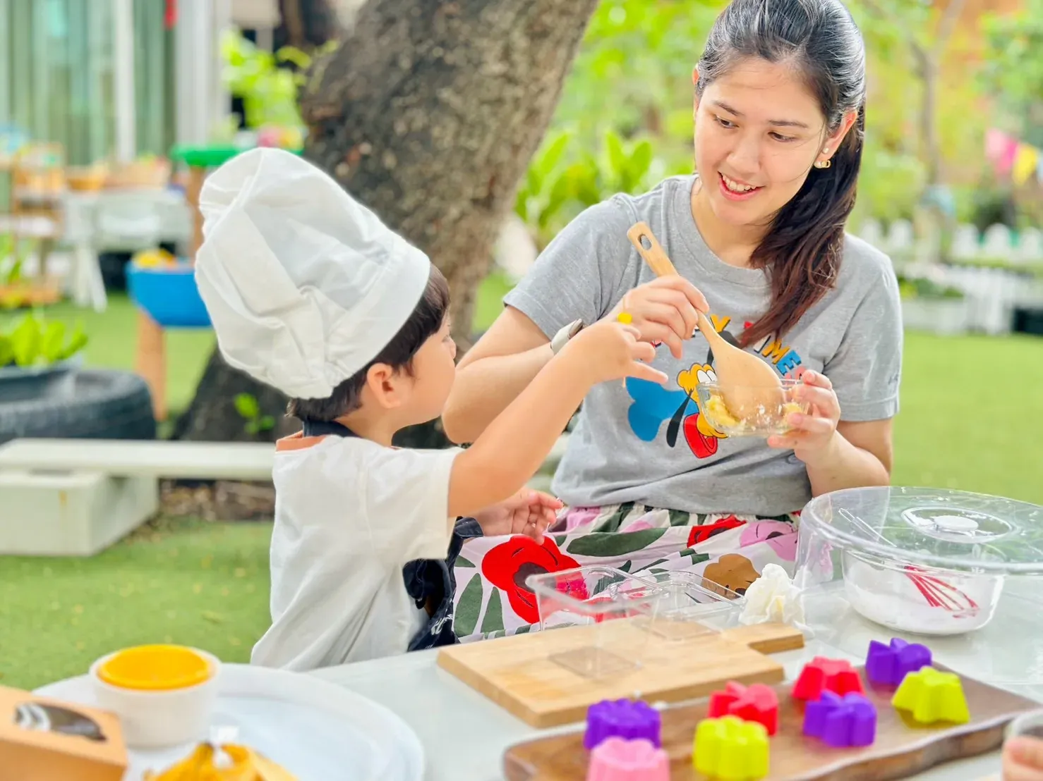 A child in a chef’s hat helping to stir a mixing bowl at the garden cooking table