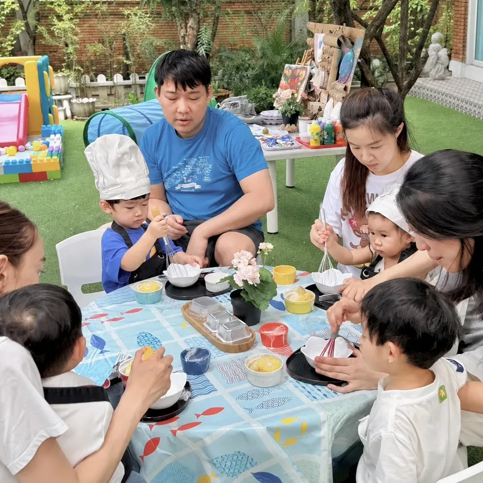 Children and parents whisking and mixing together at a garden cooking table