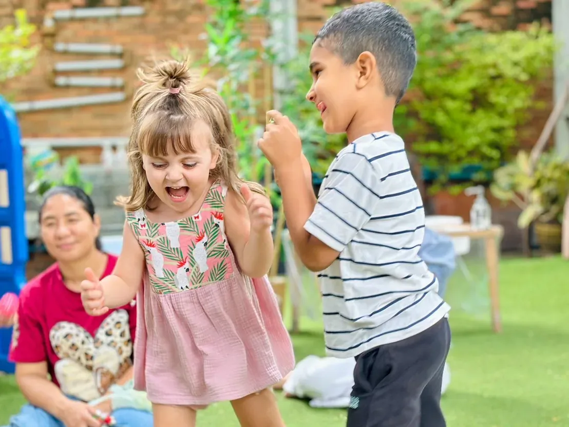 Two children laughing and dancing barefoot on the lawn