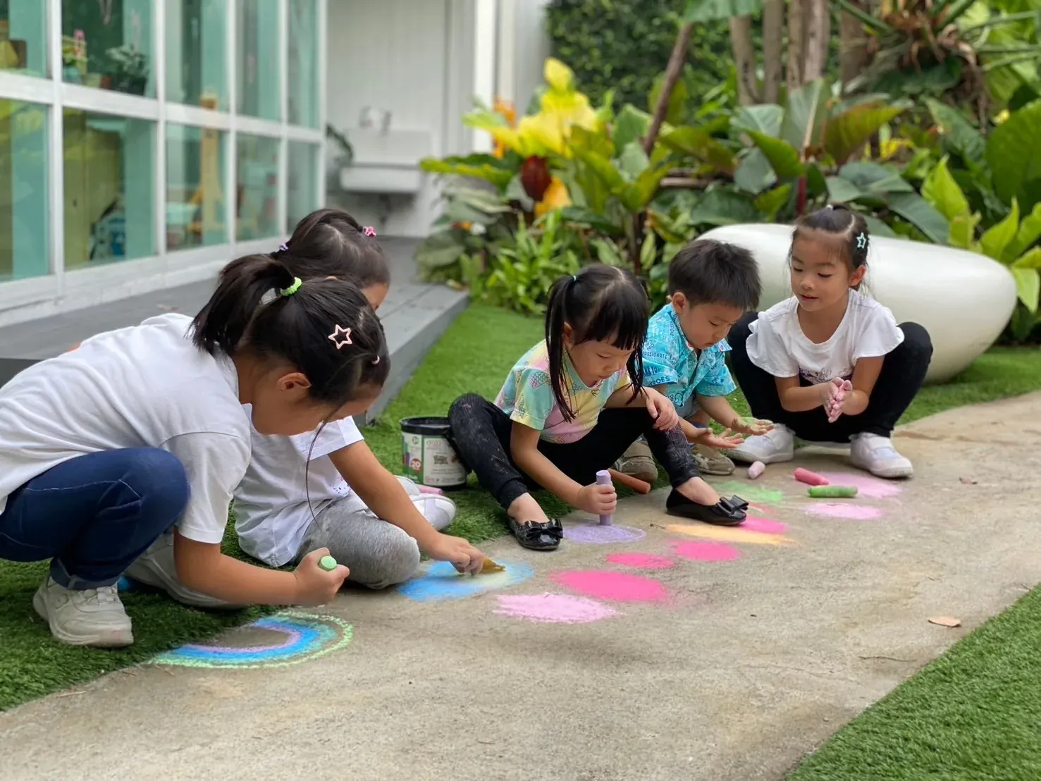 Children drawing rainbows and circles in chalk along the garden path