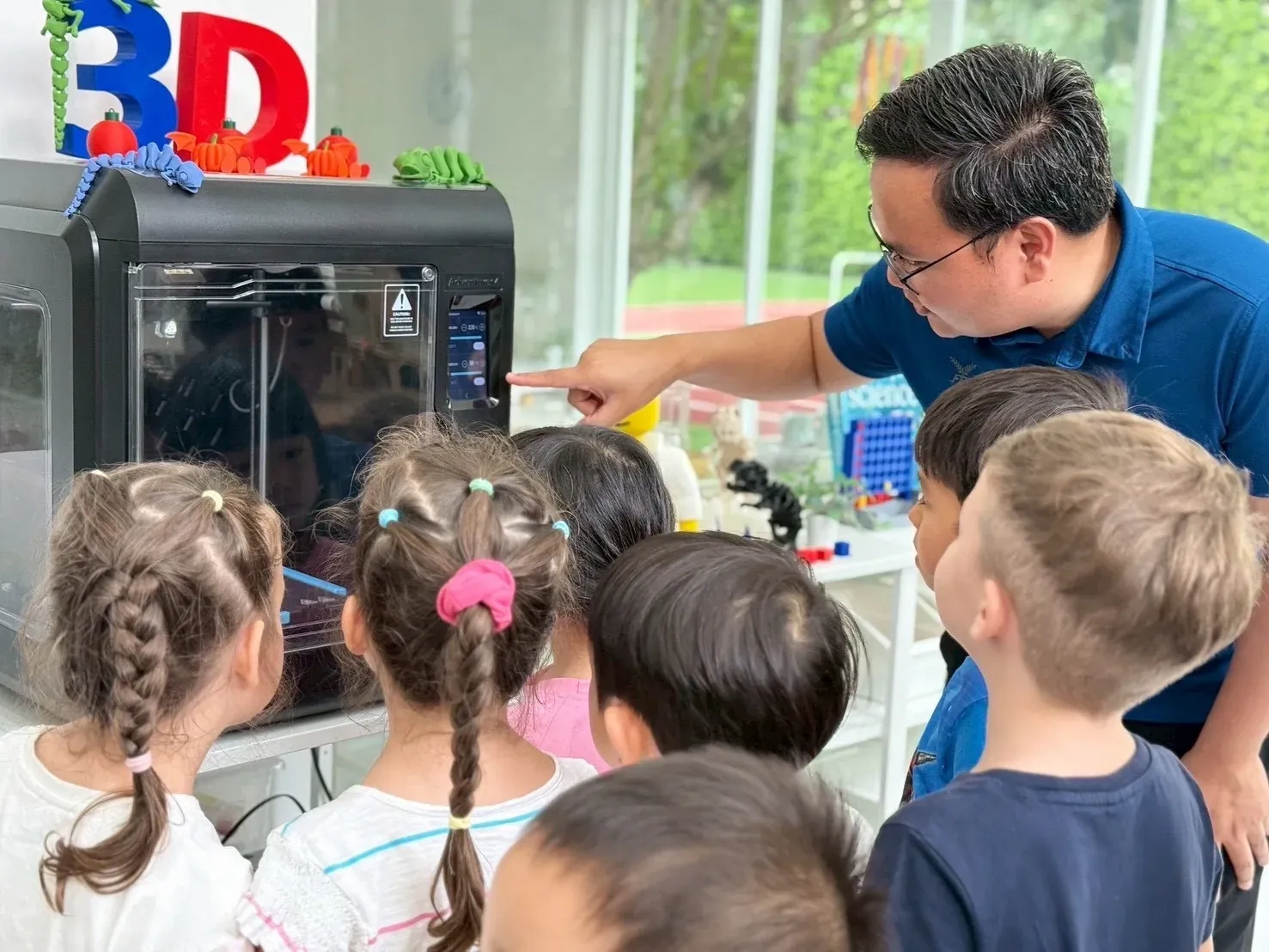 Children gathered round the 3D printer as a teacher explains it