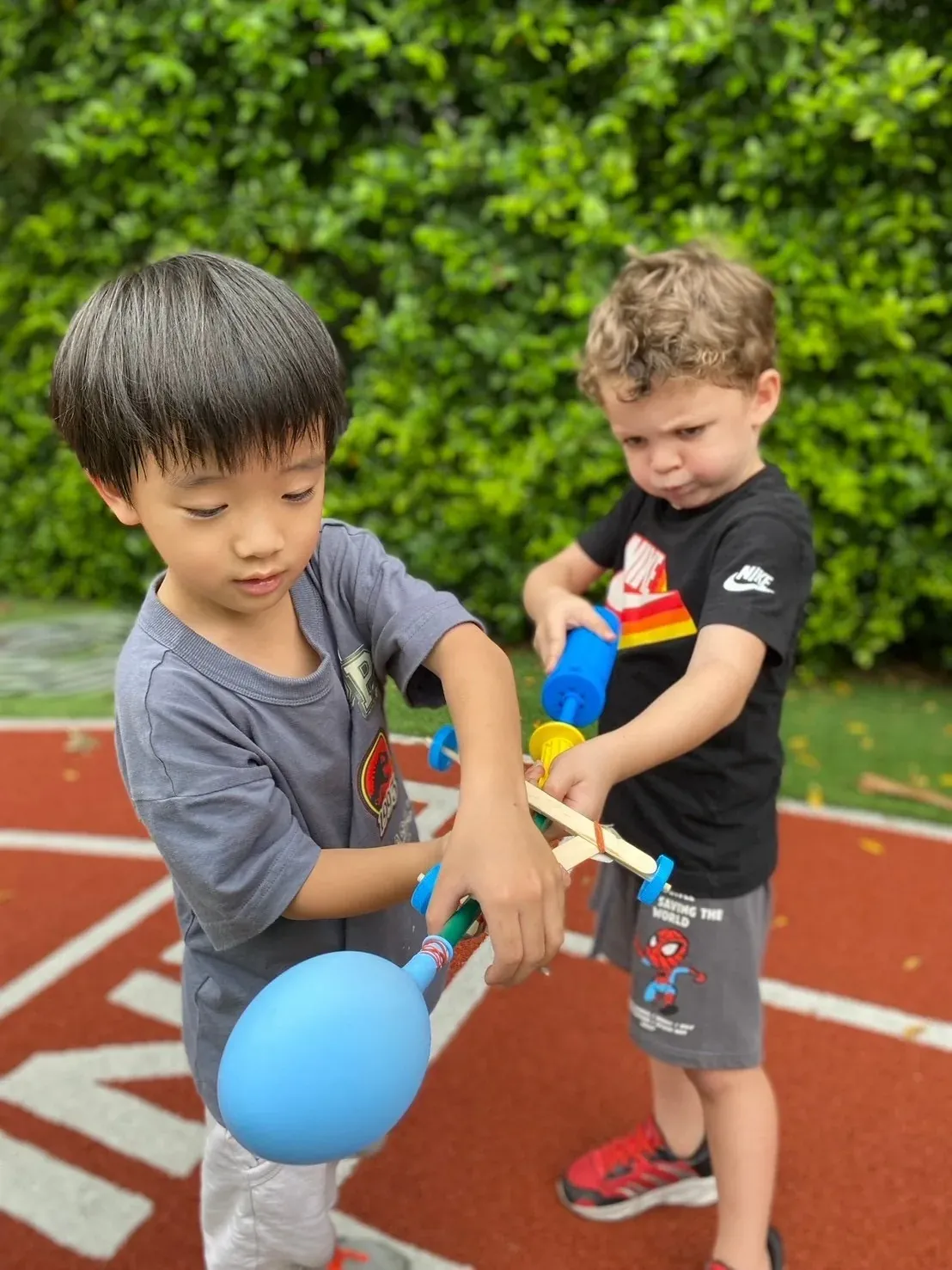 Two boys assembling a balloon-powered car from lolly sticks and wheels