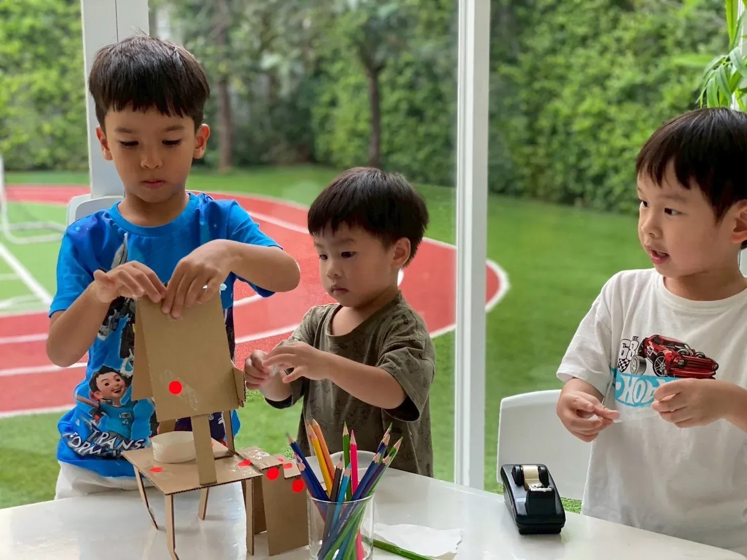 Three boys taping together the cardboard prototype of their squirrel feeder