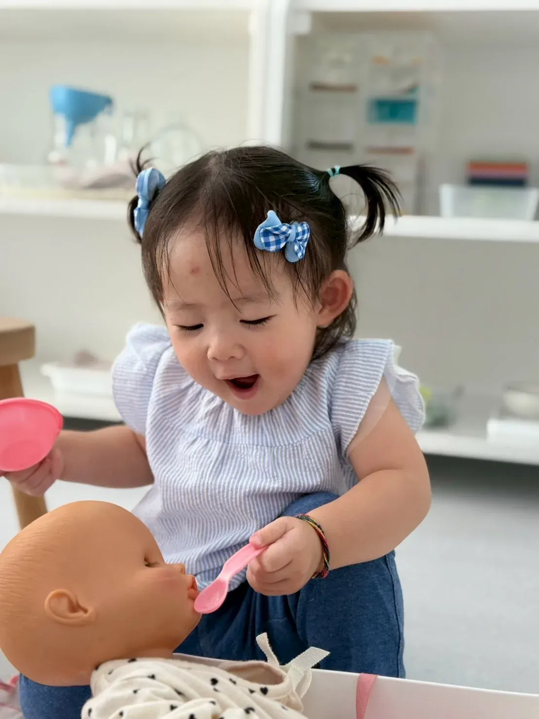 Practical Life: a toddler feeding a baby doll with a spoon