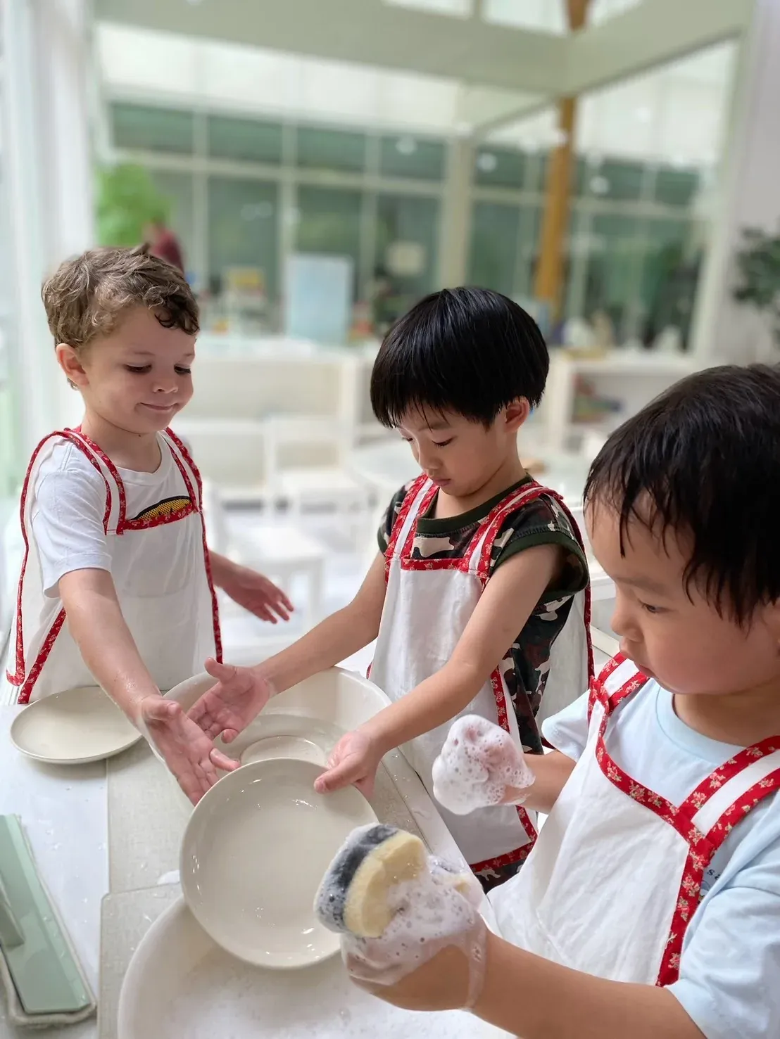 Practical Life: three boys in aprons washing up plates together