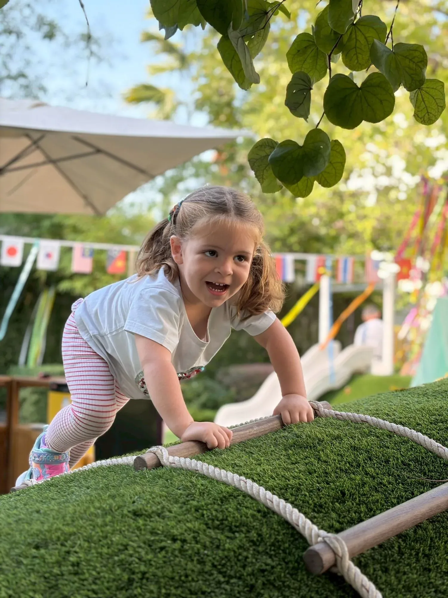 A laughing girl climbing the rope ladder up the grass hill