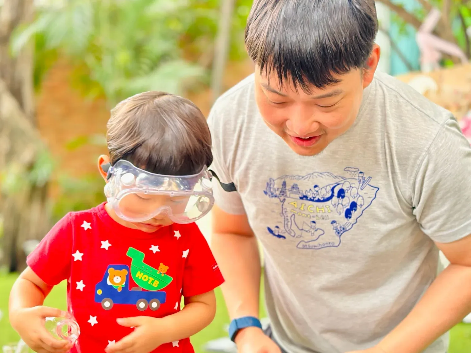A child in safety goggles exploring a dinosaur sensory tub, with a parent close by