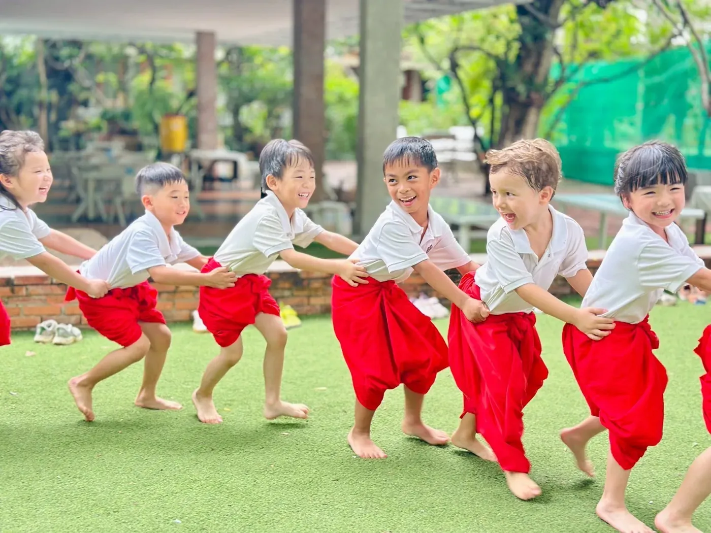 Children in traditional Thai dress playing tug of war on the school field