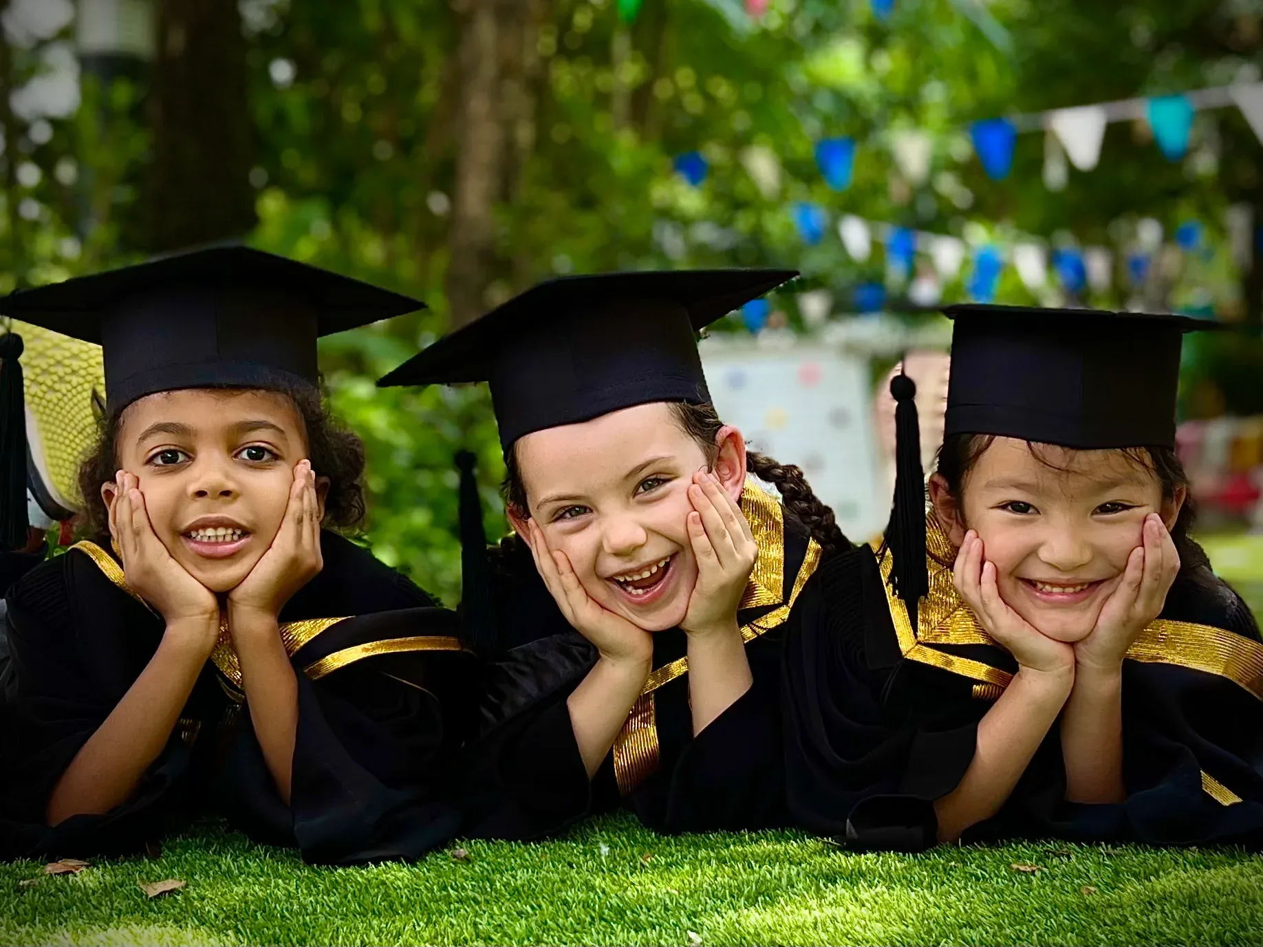 Three Kornkaew children in graduation caps and gowns, smiling on the grass