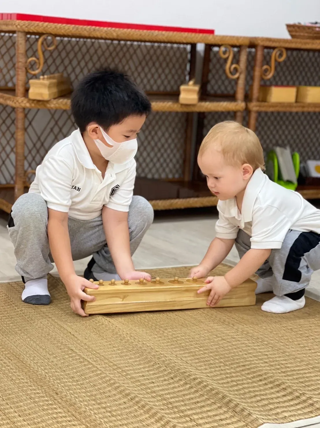Two Kornkaew children working together with a Montessori board on a woven mat