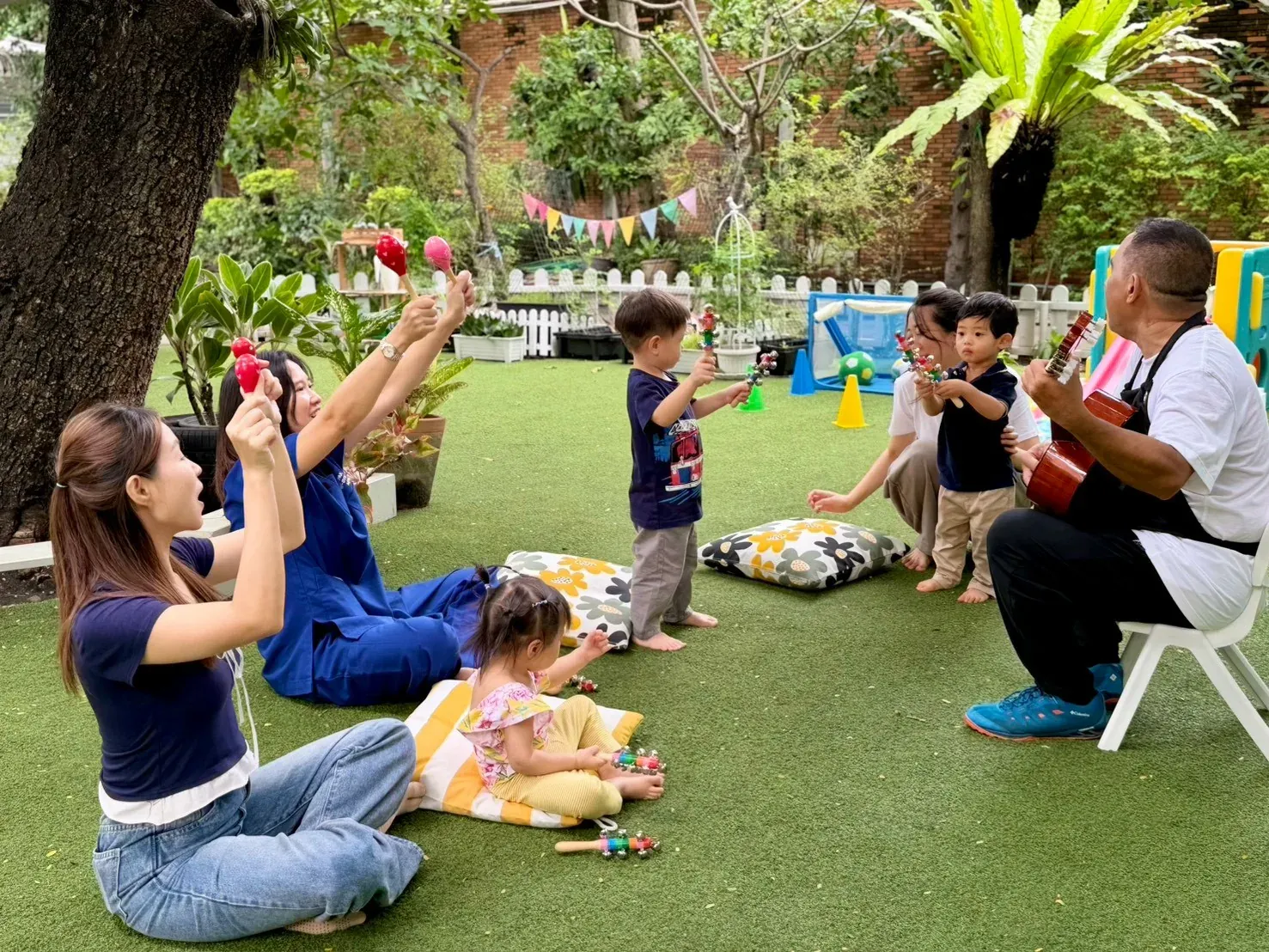 Parents, children and teachers making music on the garden lawn with shakers and a guitar