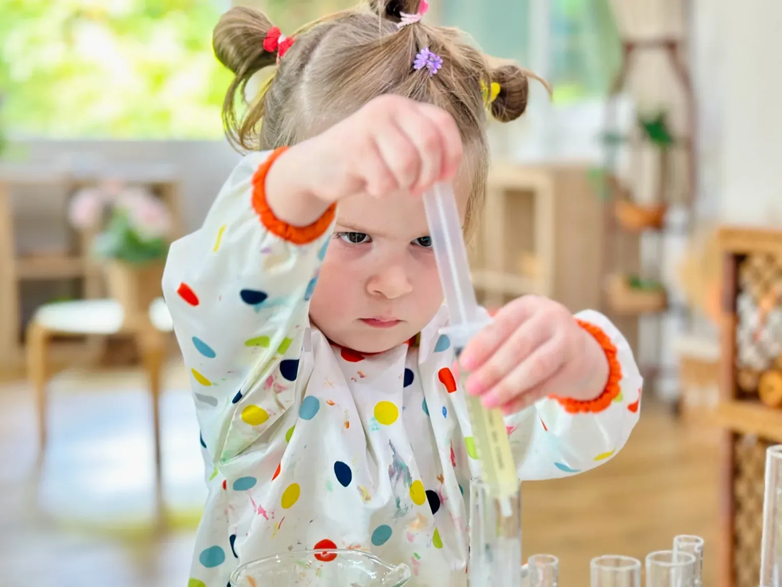 A child in a spotted painting smock using a pipette to fill a test tube