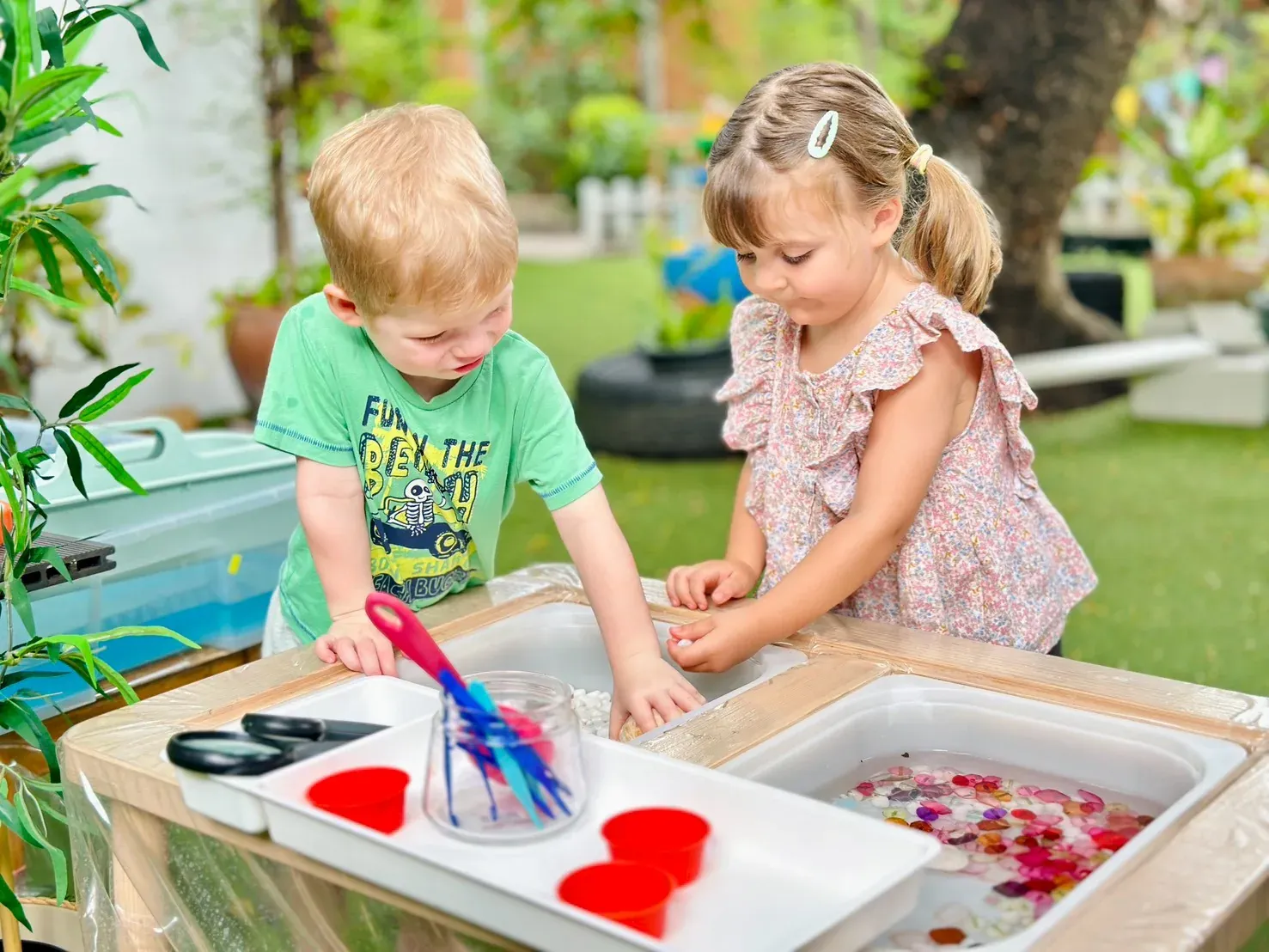 Two children sorting pebbles and petals at a sensory tray in the garden