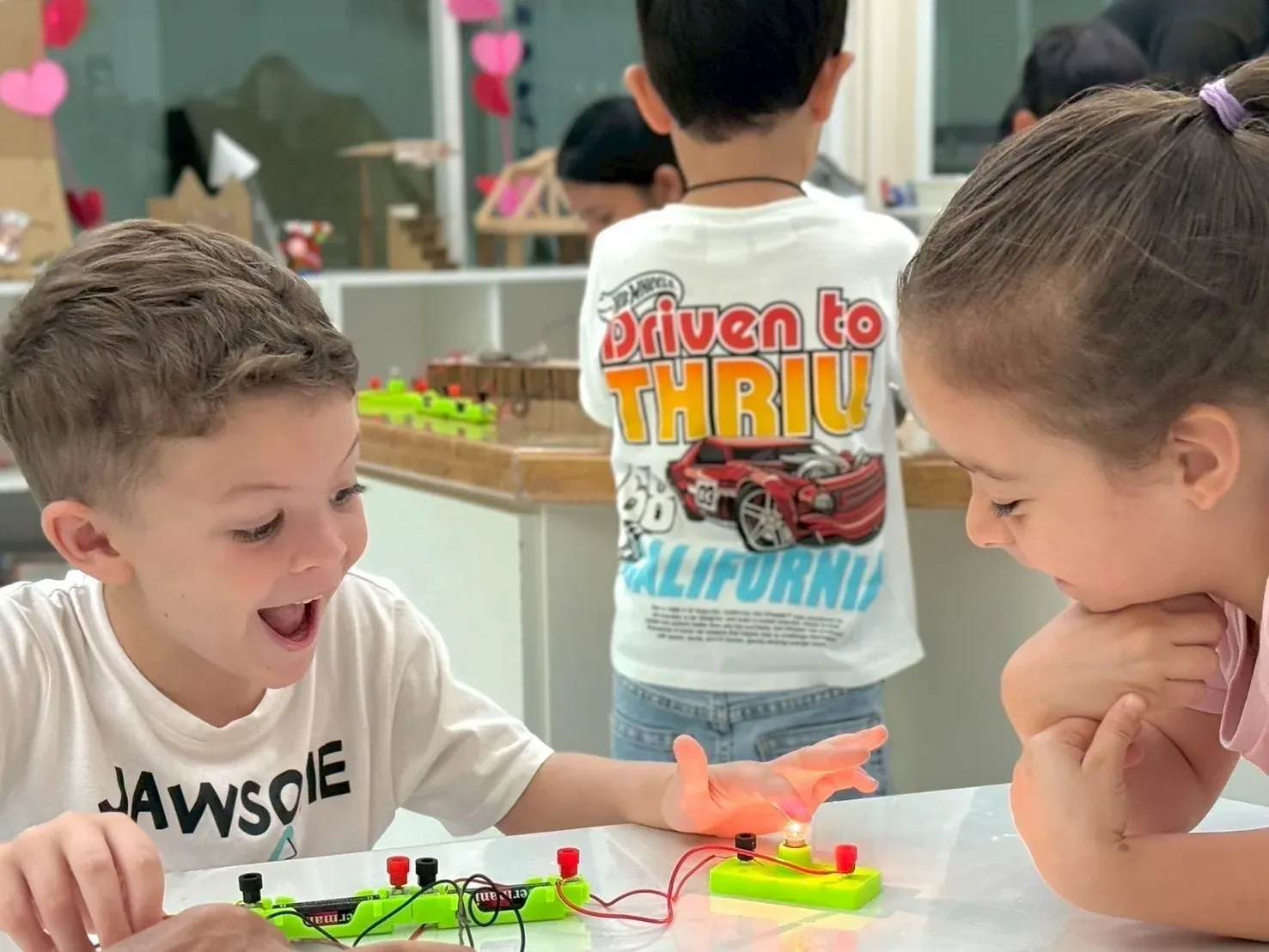 A boy lights up as the circuit he has been wiring finally works, a friend watching
