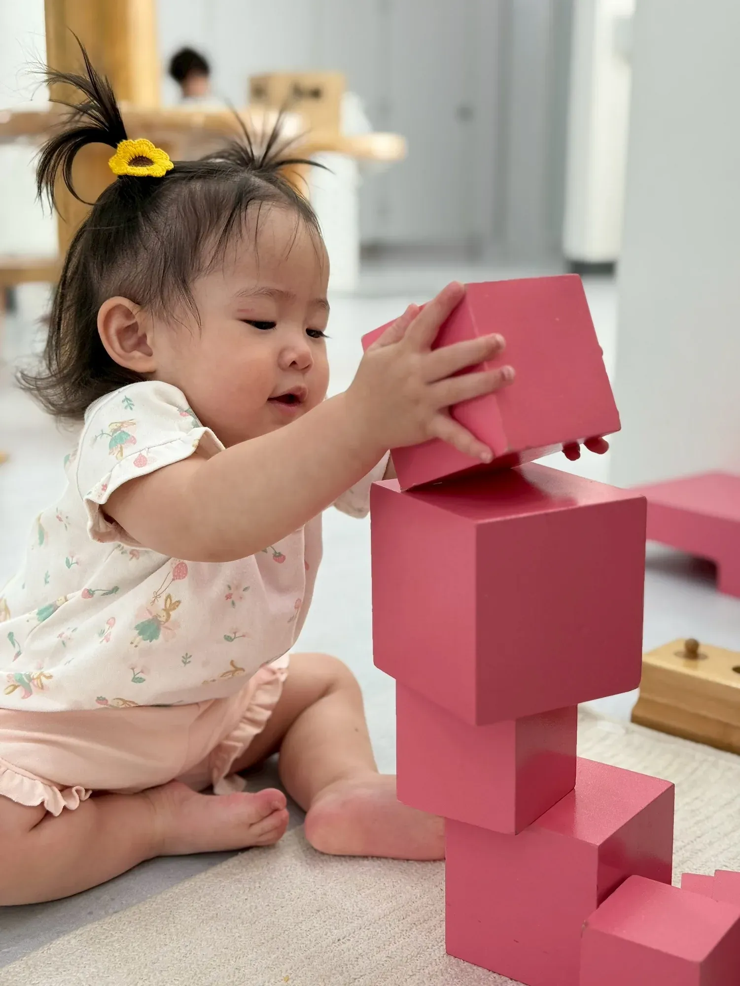 A toddler trying to balance an oversized cube on top of her pink tower
